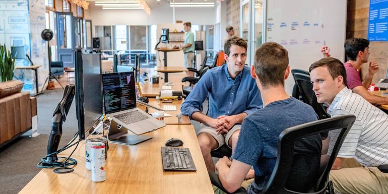 Three men i relaxed outfits having a casual meeting by an office desk