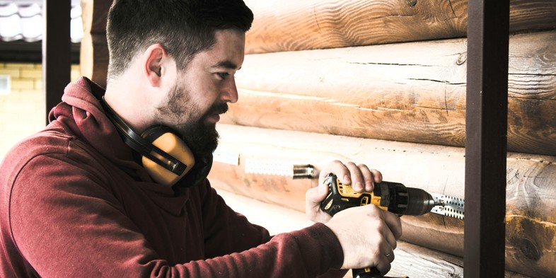 Craftsman drilling into a log house