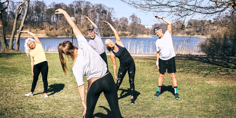 Elderly people exercising on a lawn by a lake