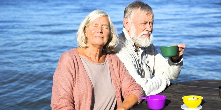 Et ældre par drikker kaffe i solen ved havet