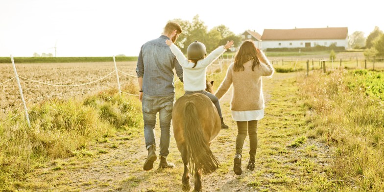 Pige rider på pony med far og søster gående ved siden af