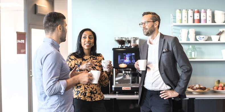 Tre kollegaer holder pause ved kaffemaskinen